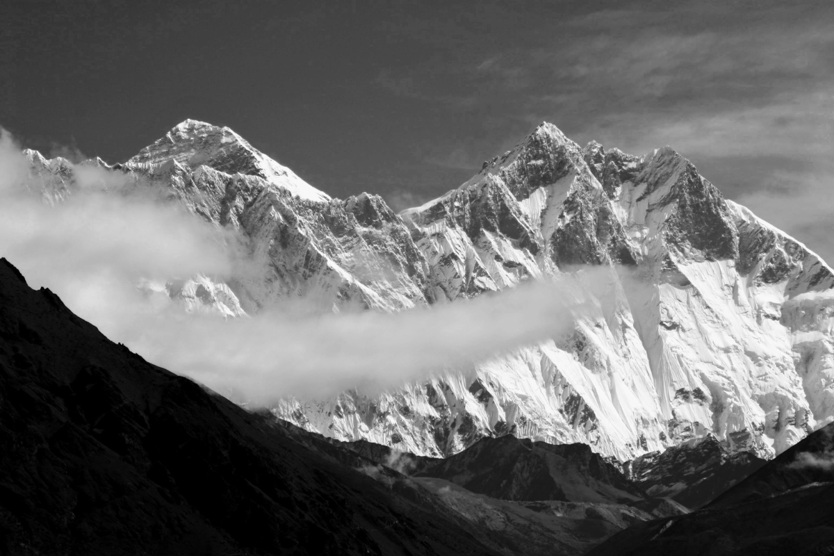 Black and white panoramic view of the Everest mountain range partially obscured by low-hanging clouds.